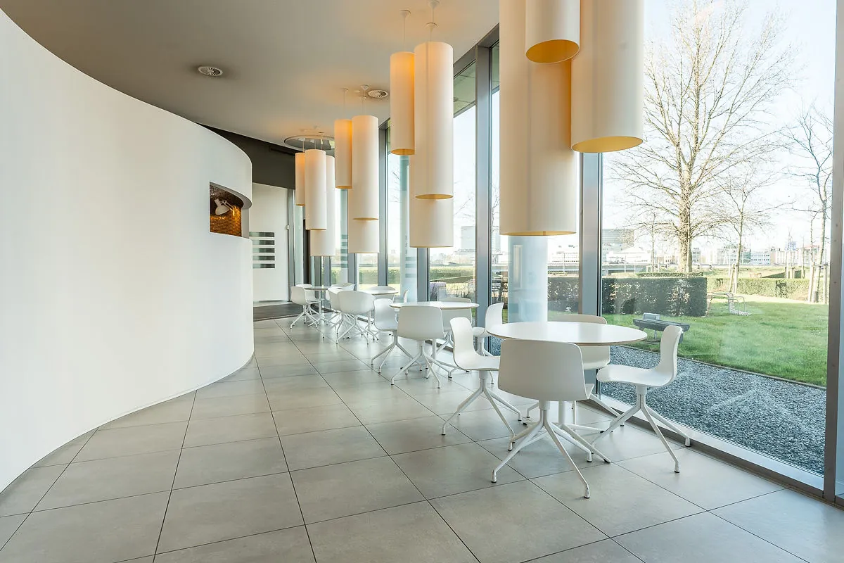 Moderne, lichte zitruimte met witte tafels en stoelen bij grote ramen in het Rivium Quadrant.